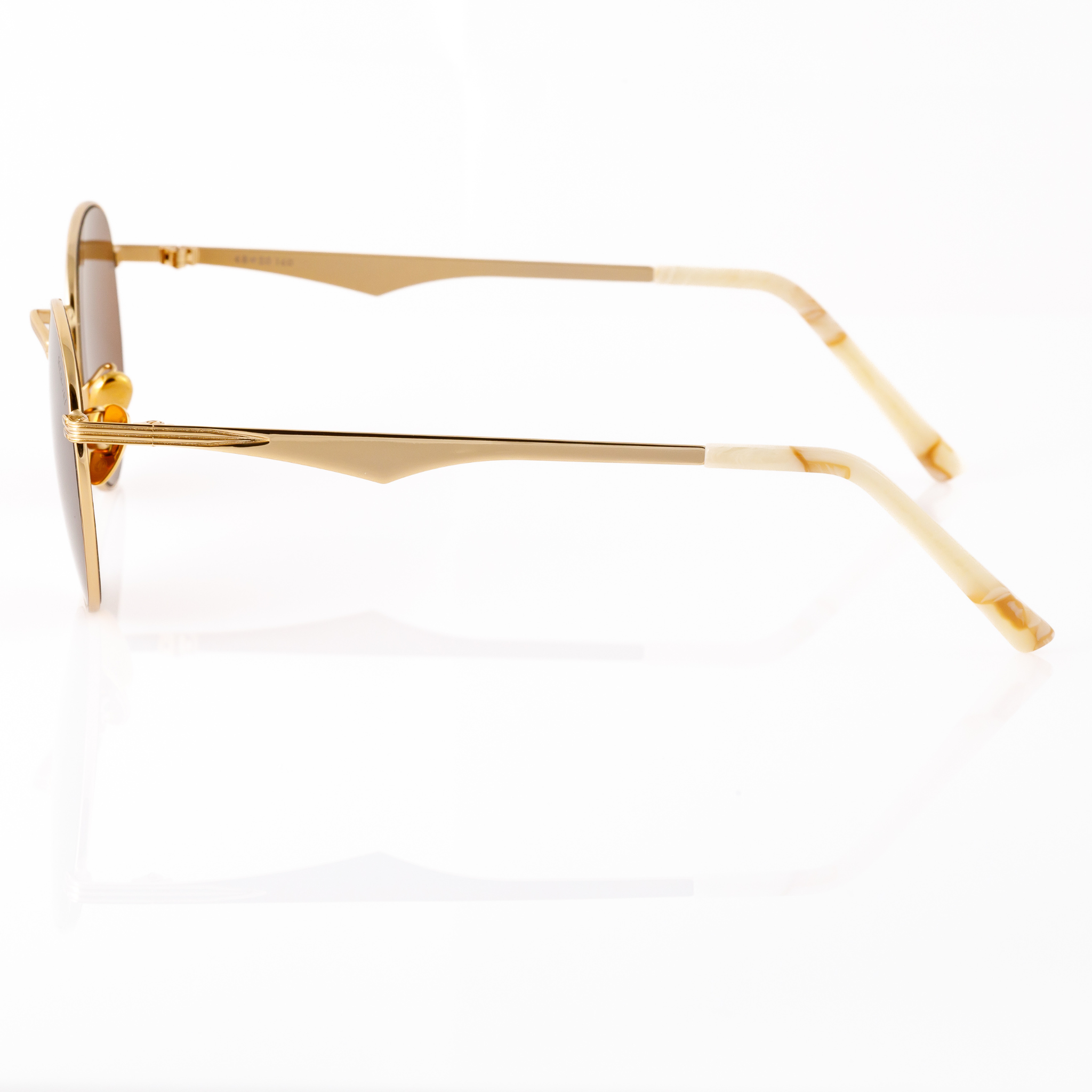 Profile view of Memorí round sunglasses in gold with warm brown lenses. Linear pointed design that wraps from hinge to temple arm is featured as well as scalloped temple arm. Ivory colored marbled mazzucchelli temple tips. Small fit sunglasses designed specifically for petite and narrow faces. Best sunglasses for small faces. 