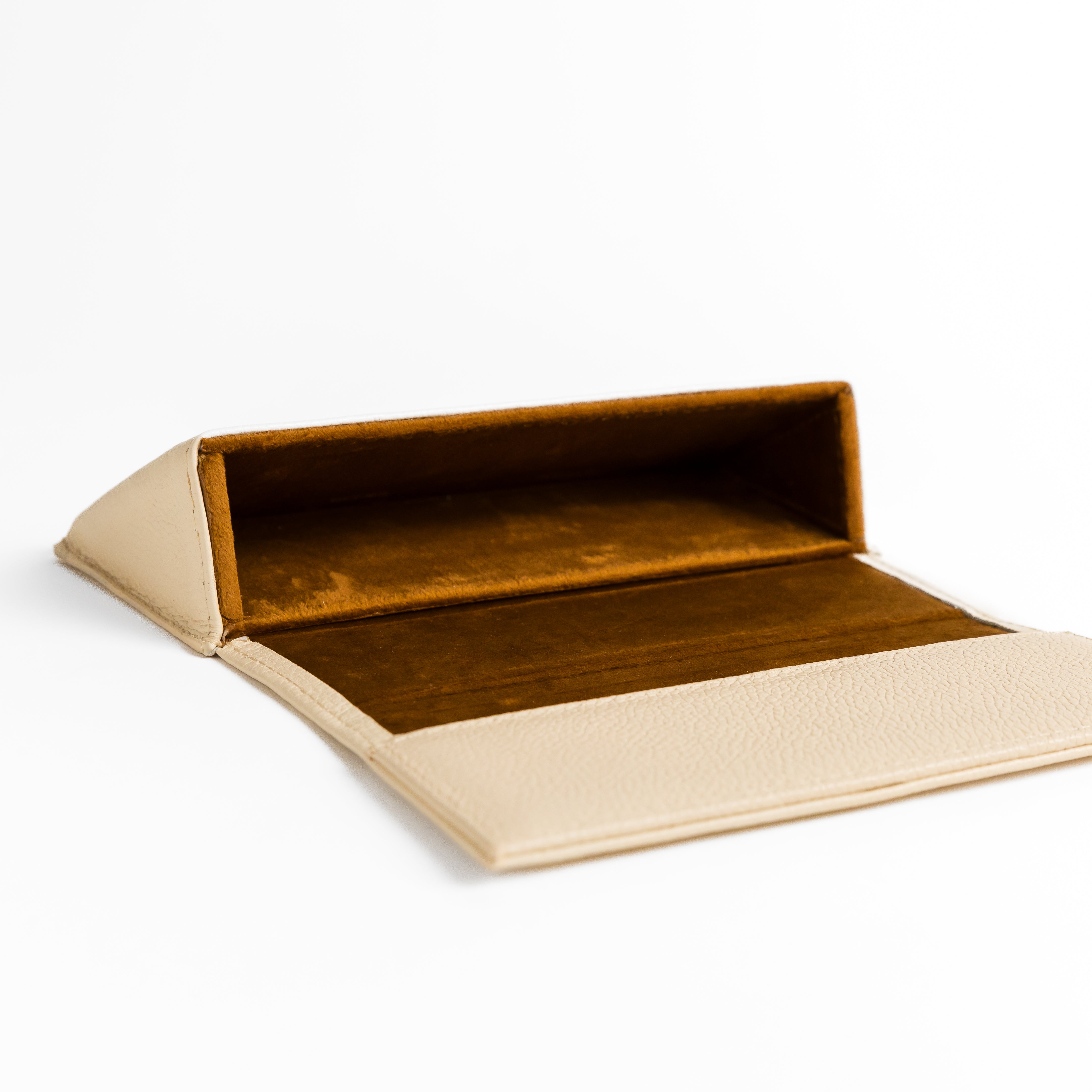 Photo of Memori hardshell leather sunglass case, laying opened on a flat surface. The warm, medium-brown velvet inner lining is exposed. This view shows the construction of the hardshell pocket the glasses fit within. The Colors and materials of this sunglass case are luxurious. Sunglass case handmade in Leon, mexico.