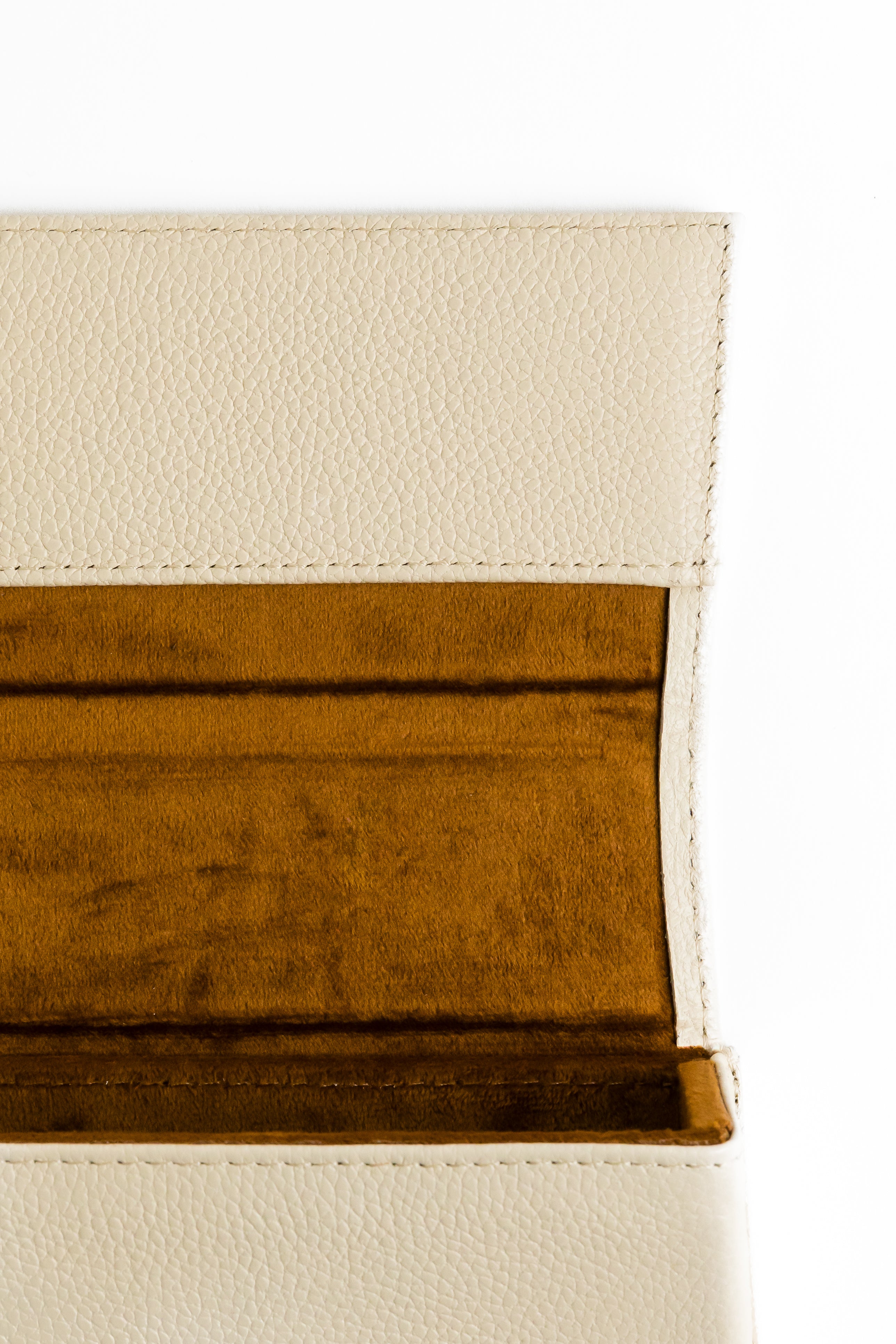 Macro view of the materials and textures of this protective leather eyewear case. Leather has a pebbled texture, and is a cream/ivory color. Inner lining is soft brown velvet, to not scratch the sunglass lenses. The photo depicts a luxurious product that is both fashion forward, and practical to protect eyewear investment.