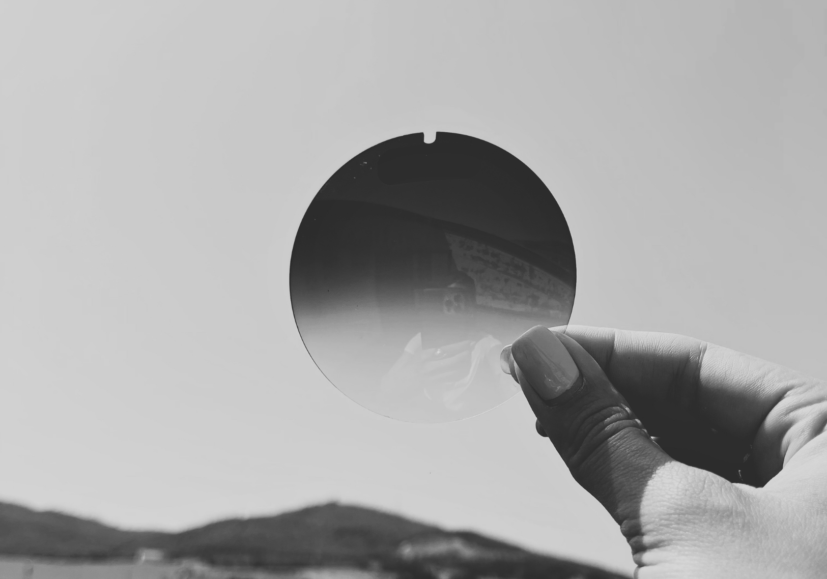 a sunglass lens being help up before being cut into the shape to fit inside the sunglass frame.