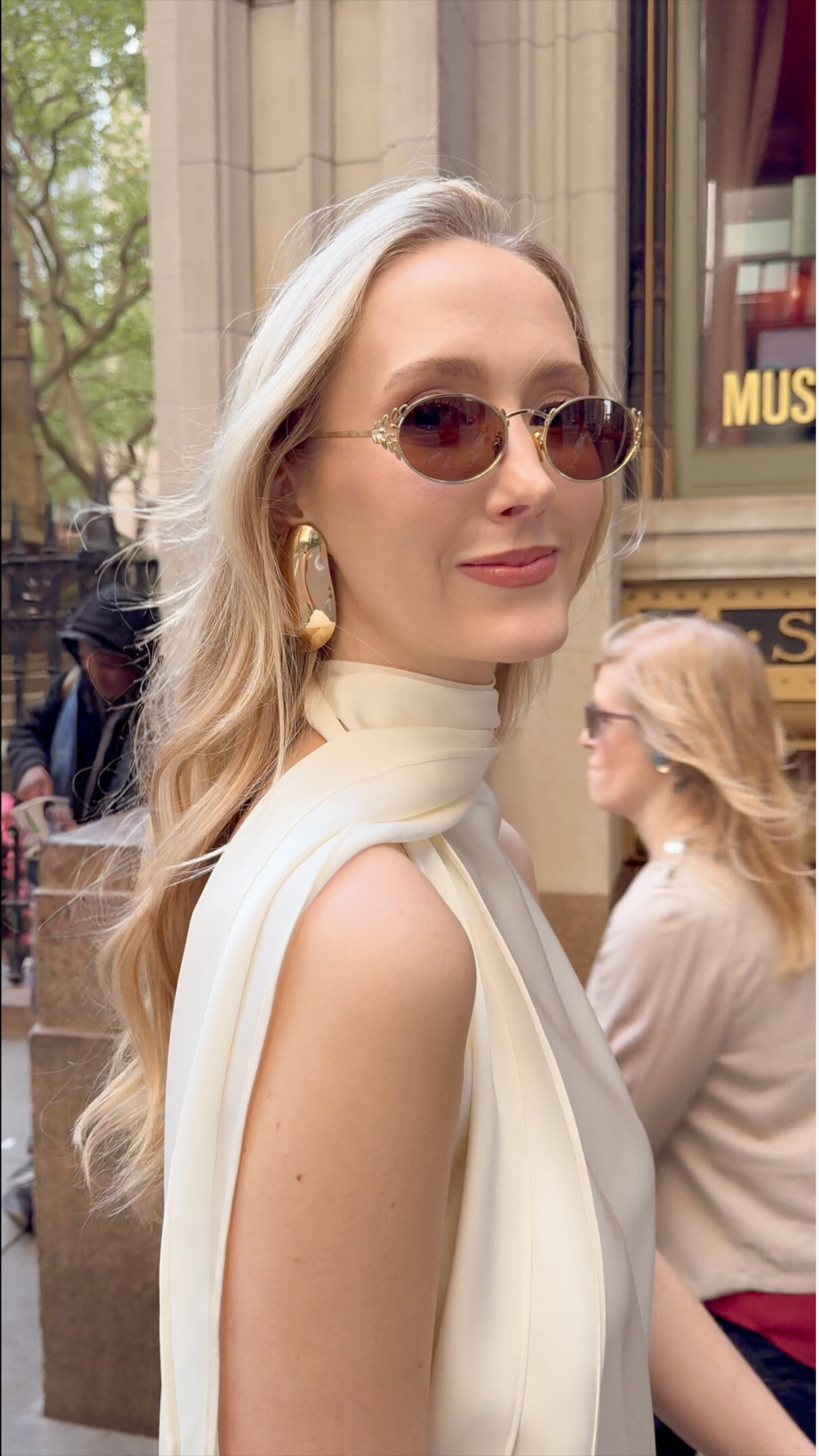 Ashlyn Lawrence, Founder of Centre Piece, wearing a top of her own design on the streets of NYC paired with oversized gold earrings and Memori Laurel oval sunglasses in gold with warm brown lenses. The overall aesthetic is very elegant and warm, and the metal leaf side details of the glasses look very elegant. 