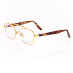 Gold-framed eyeglasses with tortoiseshell arms on a white background. Features transparent blue light blocking lenses and a sculptural gold horizontal top bar. 