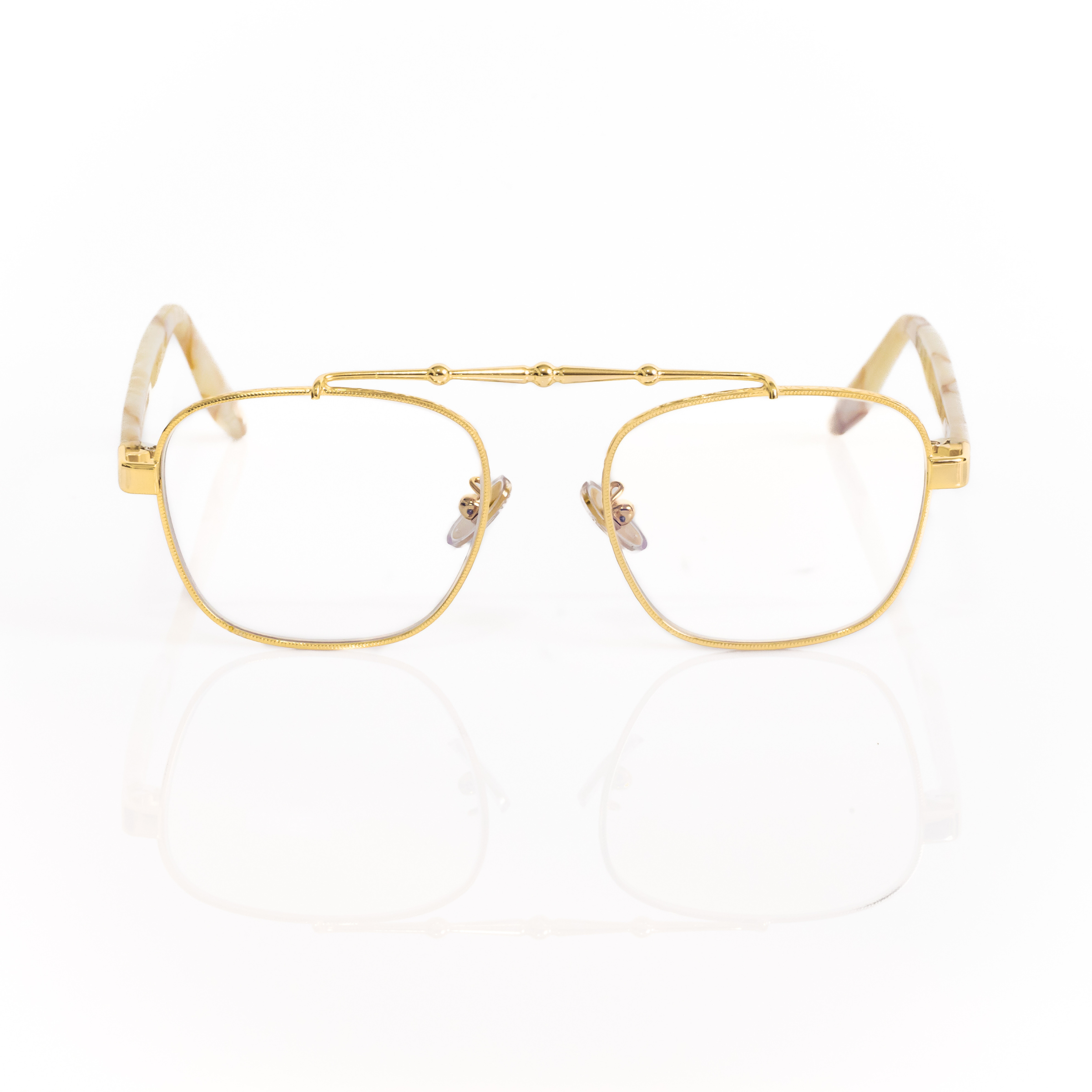 Front view of Memori Balaustra Aviator glasses on a white background. transparent lenses, gold frame, and ivory and light brown marbled acetate temple arms. Top bar has sculptural gold design details. 