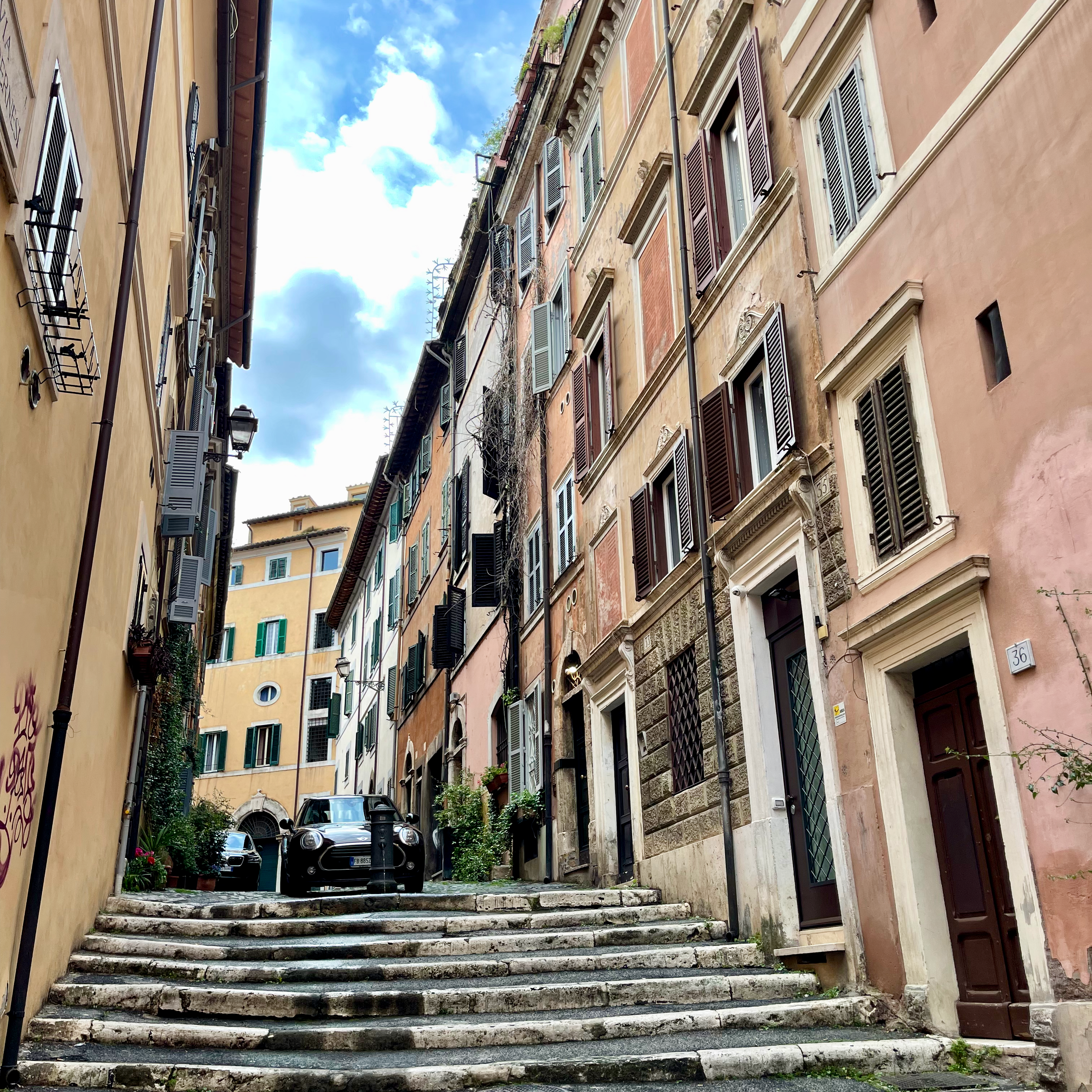 Photograph of charming alleyway in Rome, Italy. Featuring stone and concrete stairs and a parked mini cooper. 
