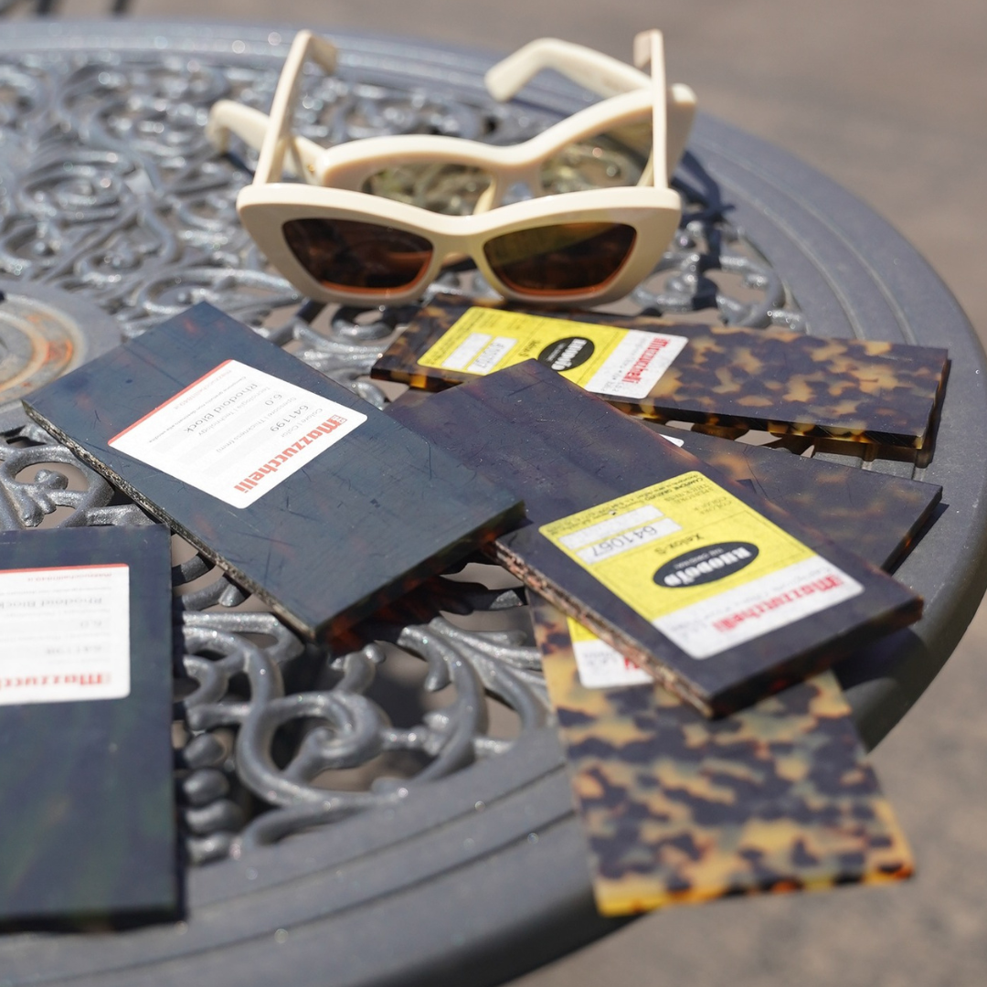 Samples of small sections of Mazzucchelli acetate sheets sitting on an outdoor table. Acetate samples are all variations of tortoise shell pattern, all handmixed in italy. 