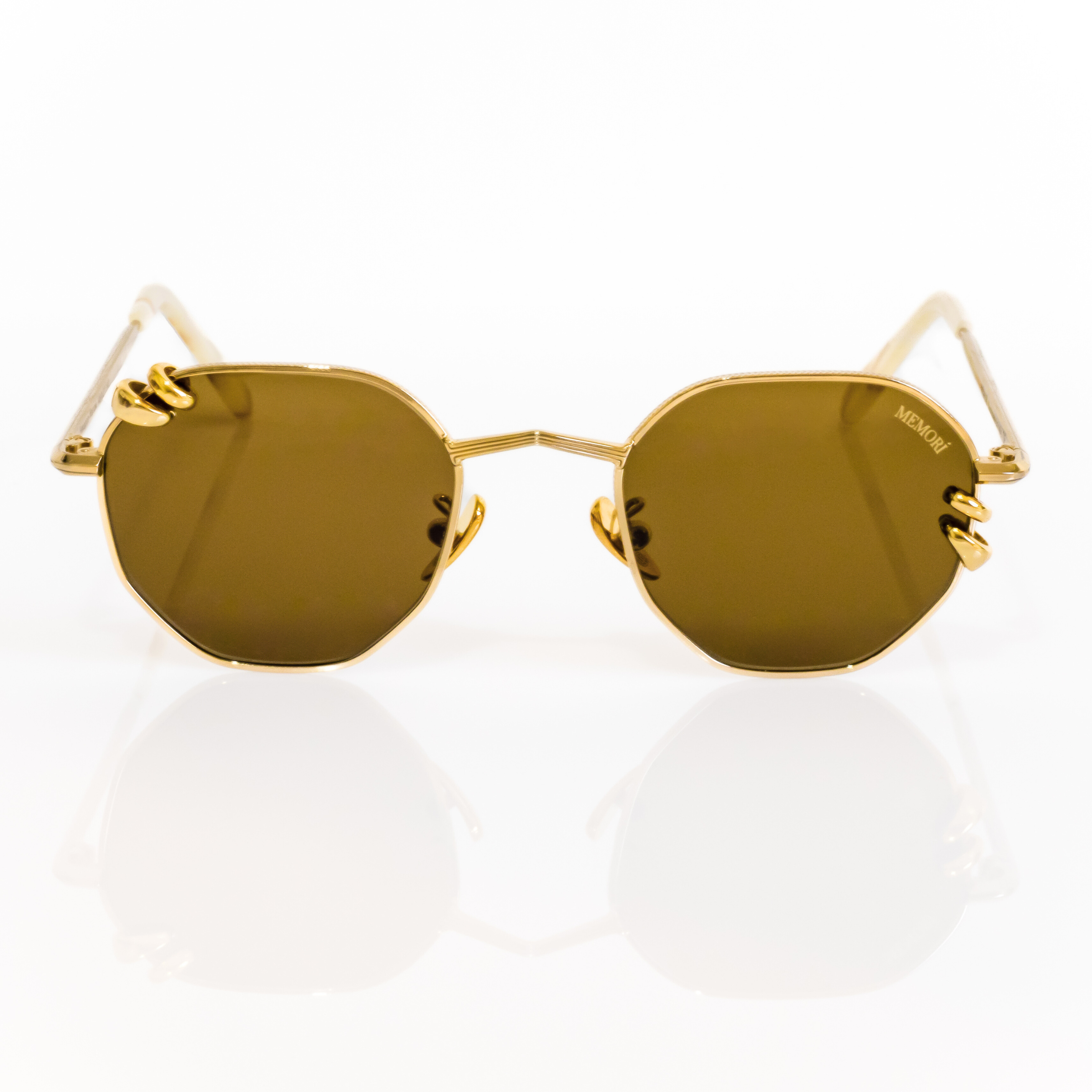 Gold metal sunglasses with brown lenses on a white background. Lens shape is geometric/hexagonal, with chunky gold hoop piercings through the lenses.Pierced sunglasses. Front view. 