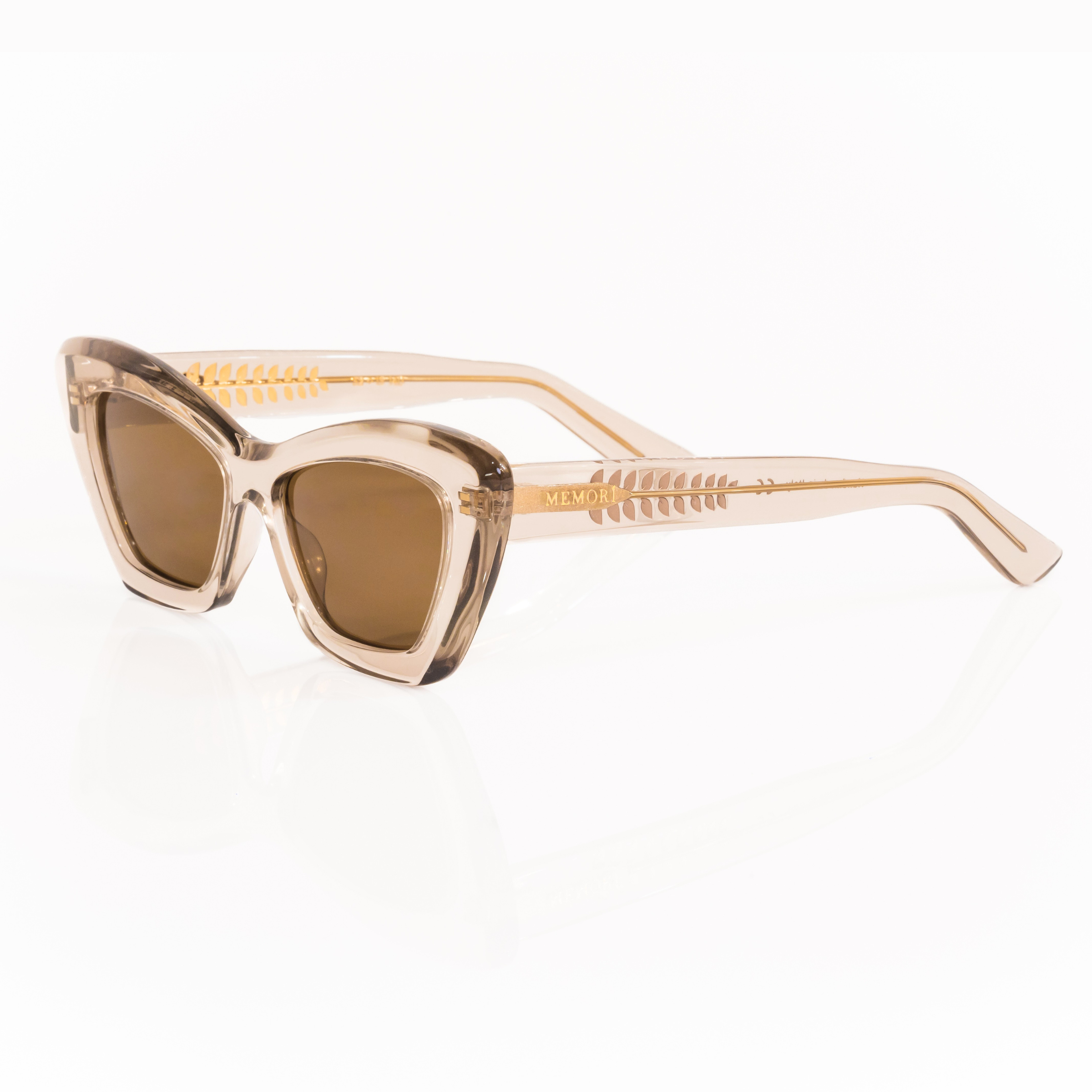 Semi-transparent Acetate sunglasses in a gray crystal color with brown lenses and a cat-eye inspired silhouette on a white background. 3/4 view shows transparent temple arms where the gold internal metal core is visible, with intricate gold leaf details down the temple arm. 