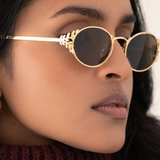 Close-up of a person with a small face shape wearing memori Laurel oval sunglasses in gold. Photo focuses on the detailed laurel leaf sides, the glasses look like a combination of sunglasses and fine jewelry for the face.