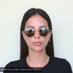 Model facing camera wearing Memorí hexagon sunglasses in gold with brown lenses. Best sunglasses for small faces. 