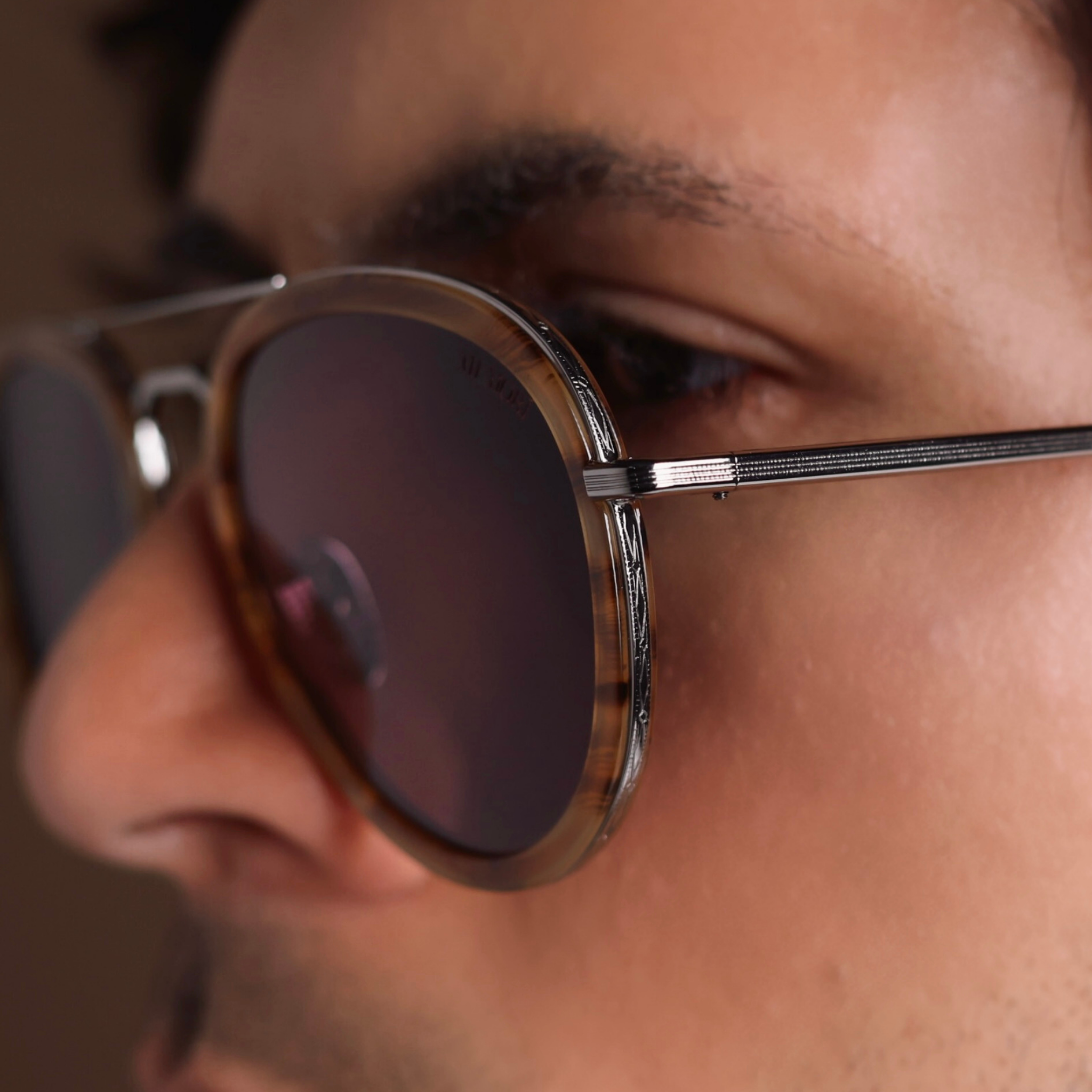 Highly zoomed in photo of memori sunglasses on a man. The photo features the geometric metal detailing around the rim of the lenses, and the tortoise acetate rim sheath. 