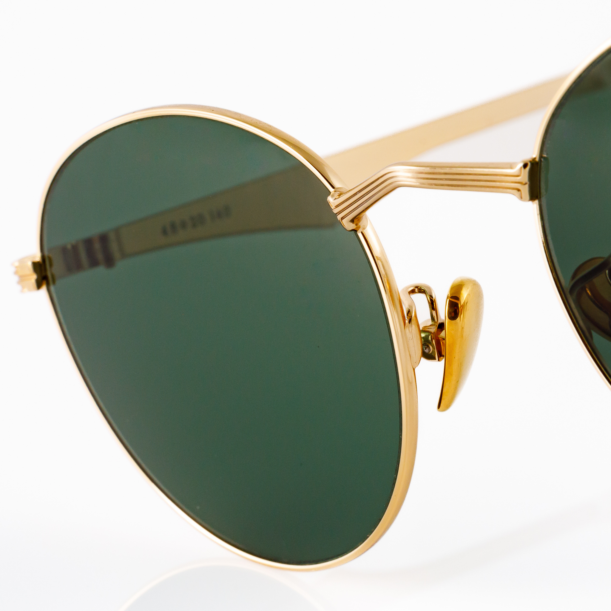 Detail shot of the metal nose bridge of a gold metal pair of sunglasses. Features a "V" shaped nose bridge which appears to be a design inspired by architectural columns, and gold nose pads which are adjustable. 