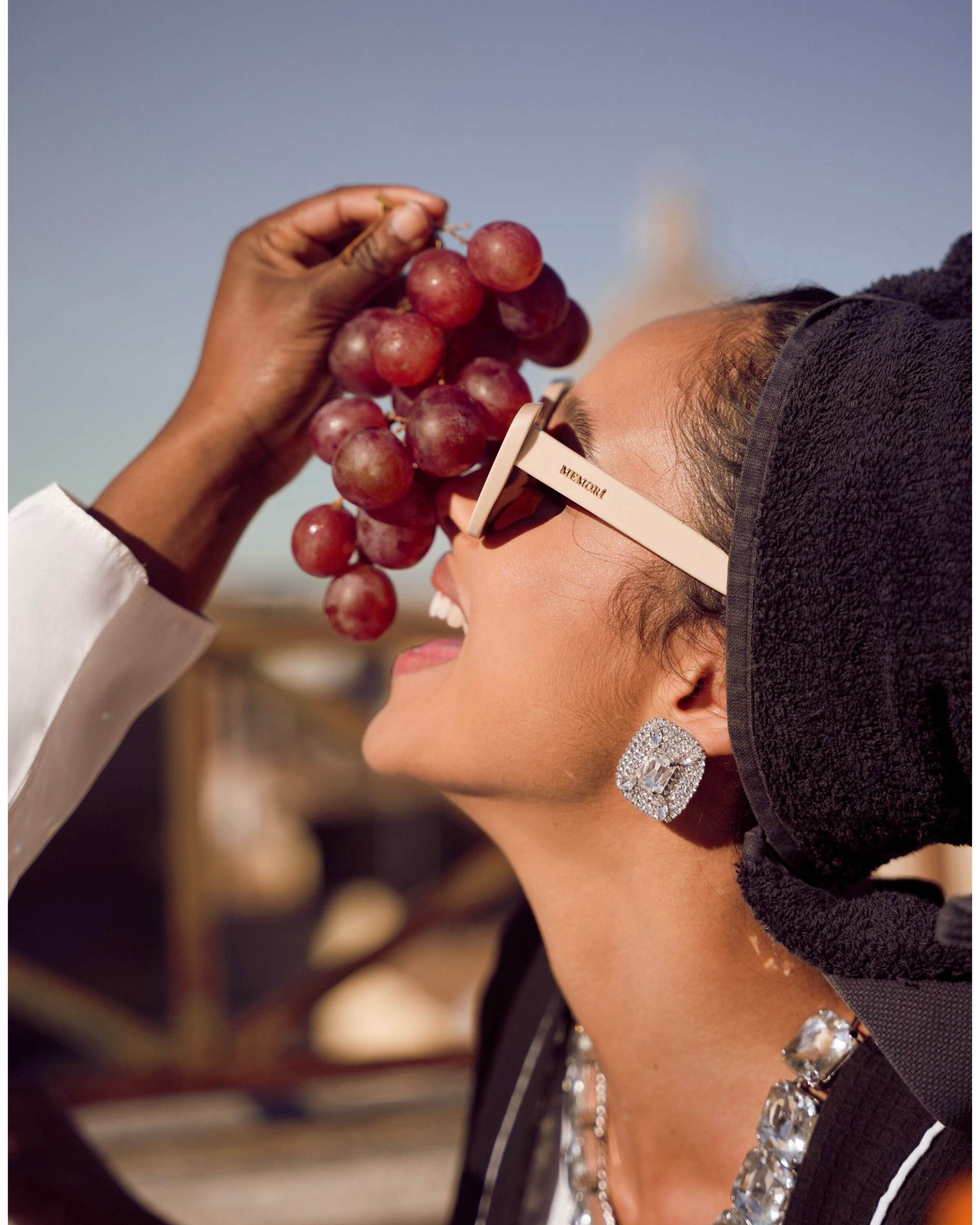 editorial image of a woman on a rooftop in Rome, Italy eating red grapes while wearing Memori ivory cat eye sunglasses, which have a small fit specifically for smaller and more petite faces