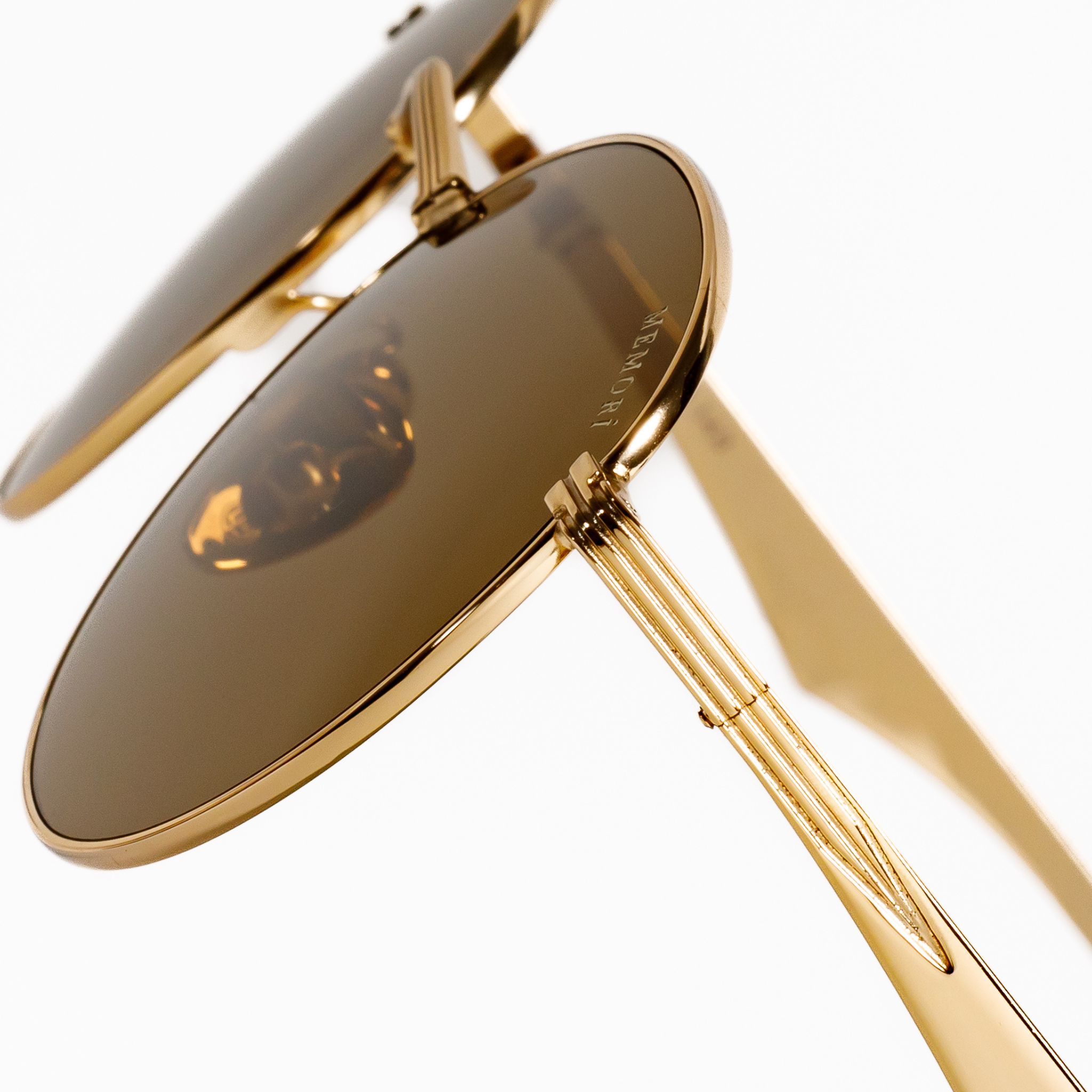 zoomed in photo of the metal details on the external corner (temple arms) of the gold round memori sunglasses. "Memorí" logo is also visible etched in the upper corner of the lens.